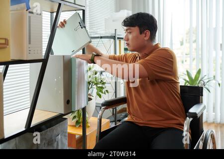 Businessman with disability talking documents folder from shelf Stock Photo