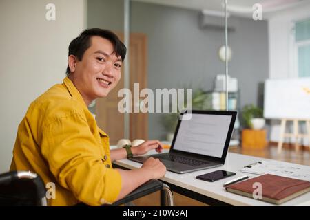 Cheerful young man with disability working on computer in office Stock Photo
