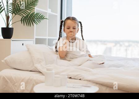 Sick child sitting on bed and covering mouth while coughing Stock Photo