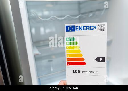 Augsburg, Bavaria, Germany - 9 September 2023: Hand holding an energy label for electric household appliances in front of a refrigerator *** Hand hält ein Energielabel für Elektro Haushaltsgeräte vor einem Kühlschrank Stock Photo