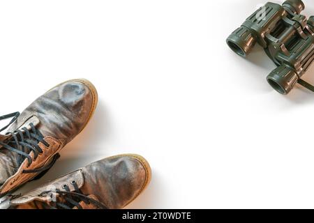 Old trekking boots and binoculars at the corners of a white background, travel concept for a hiking adventure, high angle view from above, copy space, Stock Photo