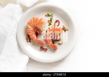 Two fried tiger prawns or shrimps with red chili pepper, garlic and herbs on a white plate, spicy seafood meal, high angle view from above, copy space Stock Photo