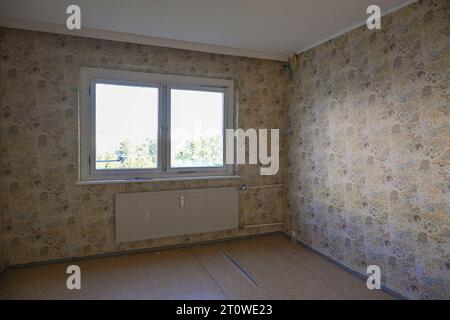 Unrenovated empty room with an old patterned wallpaper on the walls, concept for housing and shortage of affordable living space, copy space, selected Stock Photo