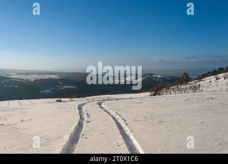 Aerial view of snow-covered mountain with tire tracks leading into the valley, Snowy mountain terrain with tire tracks in the foreground Stock Photo