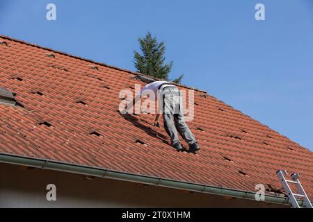 An unidentified man is preparing the roof for the installation of solar panels, red bags on the roof of the house ready for photovoltaic installations Stock Photo