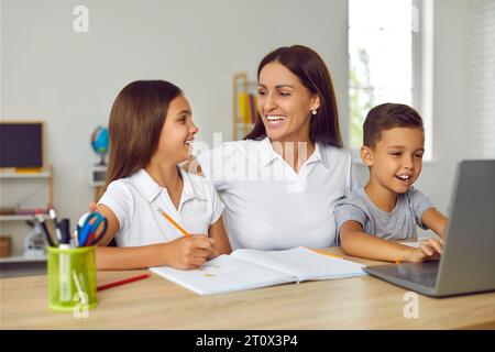 Children with their mother study at home in front of laptop, having fun doing lessons together. Stock Photo