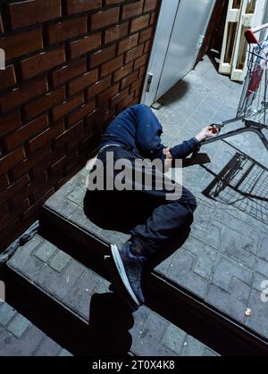 Homeless man or alcoholic sleeping on stairs near supermarket. Poor man on city street. Stock Photo