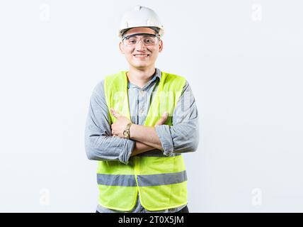 Portrait of handsome and smiling engineer with crossed arms isolated. Portrait of a young cheerful engineer in helmet and vest isolated Stock Photo