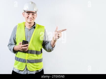 Smiling engineer holding cell phone and pointing an advertisement. Young latin engineer holding phone and pointing at blank space Stock Photo