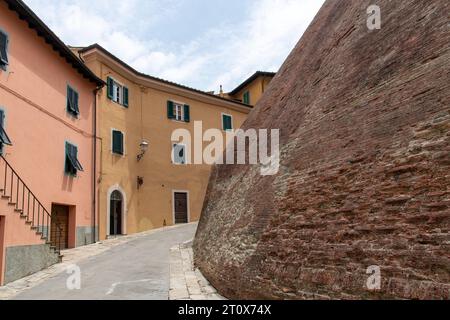 Street view in town of Lari, Italy lined with historic houses with plastered colorful walls and the fortified brick wall of the Castle of Lari (Castel Stock Photo