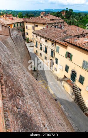 High angle street view in town of Lari, Italy lined with historic houses with plastered colorful walls and the fortified brick wall of the Castle of L Stock Photo