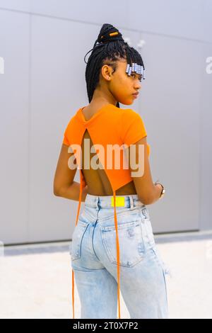 A young trap dancer with braids. Black ethnic girl with orange t-shirt and cowboy pants. Pose with his back Stock Photo