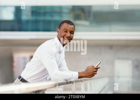 Young African American Businessman Standing Outdoors, Holding Smartphone And Smiling At Camera Stock Photo