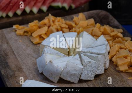 Party guests have appetizing wedge sliced cheese wheel set up on a buffet table. Stock Photo