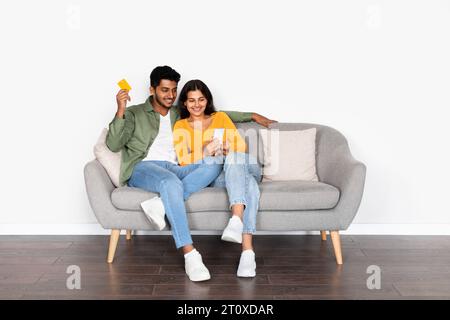 Indian couple sitting on sofa using cellphone and credit card Stock Photo