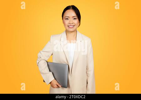 Millennial asian woman in suit looks thoughtfully at laptop Stock Photo