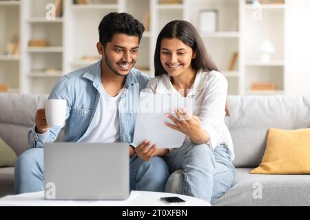 Happy indian couple attentively checking documents and using laptop Stock Photo