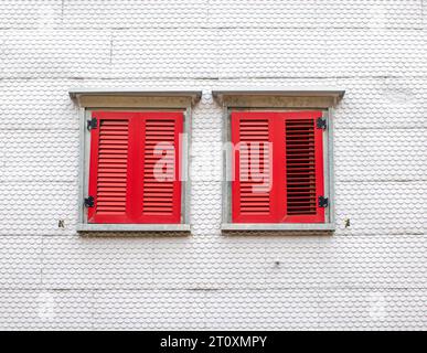 two red wooden shutters on a white facade in the style of wooden shingle siding Stock Photo