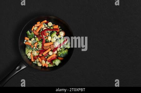 Frying pan with sliced frozen vegetables mix on black background. Vegetable mix salad. Top view, flat lay. Copy space. Stock Photo