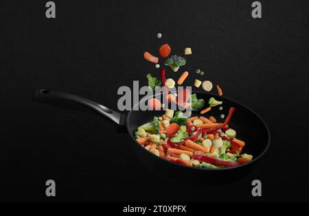 Falling frozen vegetables in a frying pan on a black background. Vegetable mix flying down. Healthy natural food. Stock Photo