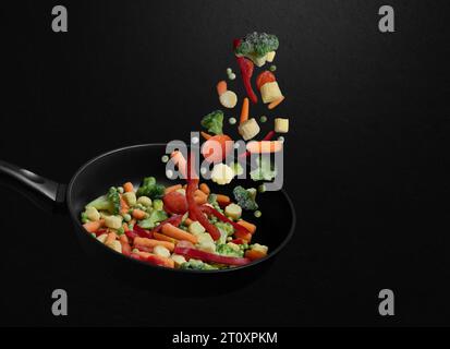 Falling sliced vegetable mix on a frying pan. Flying down frozen vegetables on black background. Natural organic food. Copy space. Stock Photo