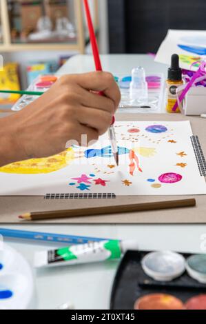 This close-up of hand holding a brush and painting with watercolor on a table. Also a beautiful and colorful abstract design. Very colorful Stock Photo