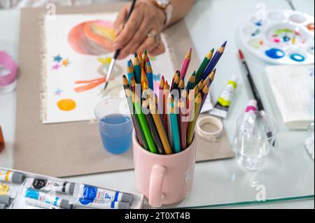 This close-up photo shows a group of colored pencils in a cup on a wooden table. The pencils are arranged in a rainbow of colors. Stock Photo