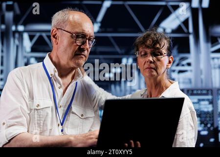 Old data storage company executives doing diagnostic assessments on high tech workspace servers. Engineers during yearly maintenance looking for potential system shortcomings Stock Photo