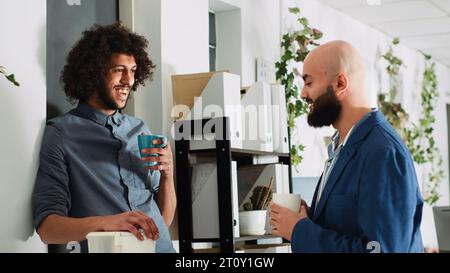 Colleagues relaxing on coffee break, having conversation and enjoying laugh together. Two business partners talking to each other before starting to work on startup development. Stock Photo