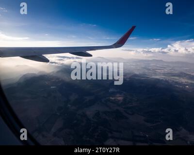 view thru the window of a passanger jet airplane flying from Bogotá Colombia showing the wing of the plane and the afternoon light Stock Photo