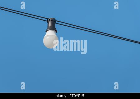 Wired light bulb hanging over blue sky in summer outdoors Stock Photo