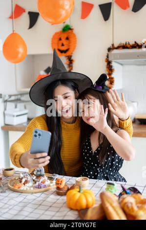 A cute and happy young Asian girl in a Halloween costume is having fun, taking selfies or taking video with her mom, and celebrating Halloween at home Stock Photo