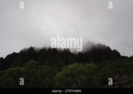 Dramatic moody view of rocky spiky ridge disappearing in low hanging clouds, cloudy weather in cradle mountain, tasmania, australia Stock Photo