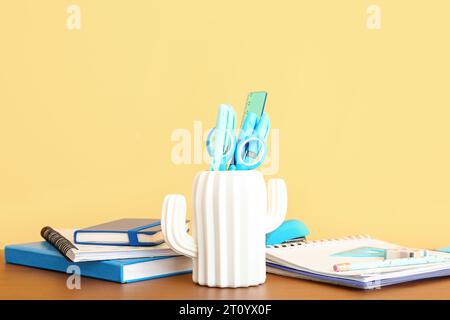 Holder with different stationery and notebooks on wooden desk Stock Photo