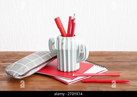 Holder with different stationery and notebooks on wooden desk Stock Photo