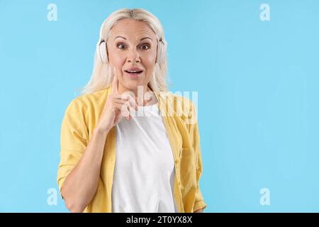 Thoughtful mature woman in headphones on blue background Stock Photo