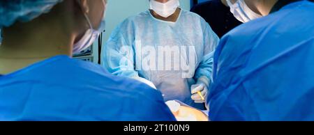 A team of surgeons in blue sterile gowns performs a surgical operation. Selective focus. Surgical instruments in the hands of a doctor. Stock Photo