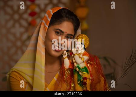 Close-up portrait of smiling woman with a statue of Lord Krishna Stock Photo