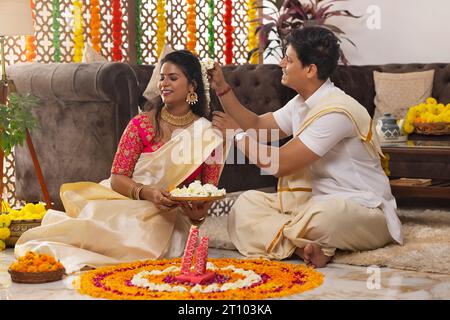 Loving husband putting flower in his wife's hair while decorating house on Onam Stock Photo