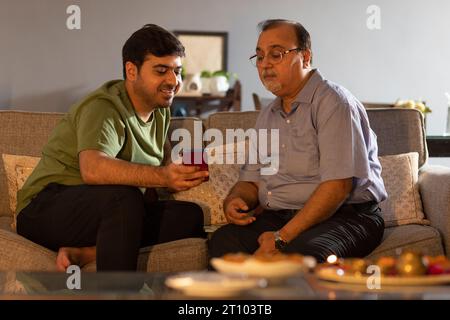 Father and son watching mobile phone while sitting on sofa at home Stock Photo