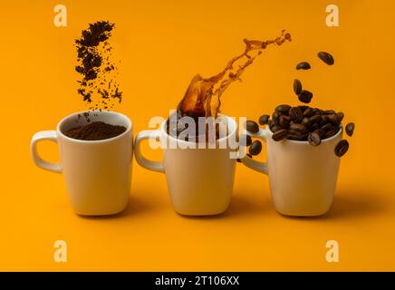 Three cups of coffee with ground coffee, beans and liquid on yellow background making big splashes. Stock Photo