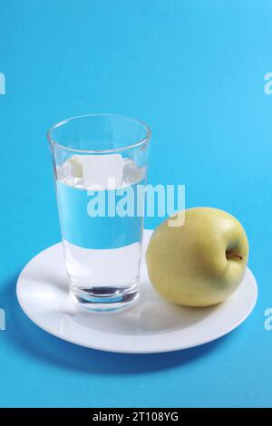 Green apples and glass of water on a plate on blue background Stock Photo