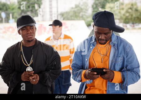 Two young African American male rappers in caps and jackets moving forwards while one of them holding walkman and listening to music Stock Photo