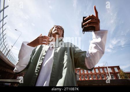 View from below of young excited African American man with walkman in hand performing hip hop against blue sky in urban environment Stock Photo