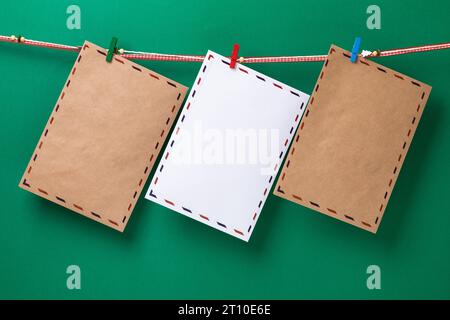 Three envelopes for Santa Claus, attached with clothespins, hanging on a rope on a green background, template for designer Stock Photo