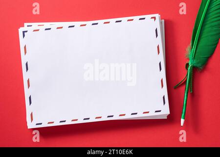 A stack of white empty mailing envelopes and a pen in the shape of a feather on a red background, template for the designer Stock Photo