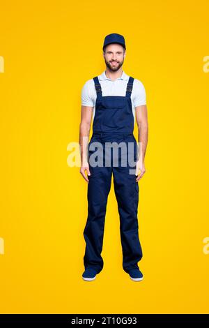 Full size fullbody portrait of attractive cheerful deliver in blue uniform with stubble looking at camera holding, isolated on grey background Stock Photo