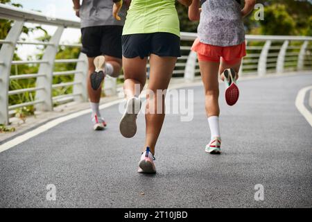 three young asian women female joggers exercising outdoors together in city park Stock Photo