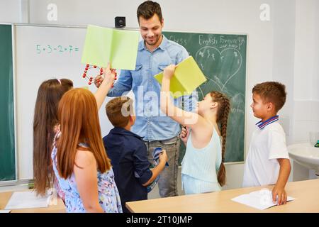 Schoolkids showing notebooks to male teacher standing in classroom Stock Photo