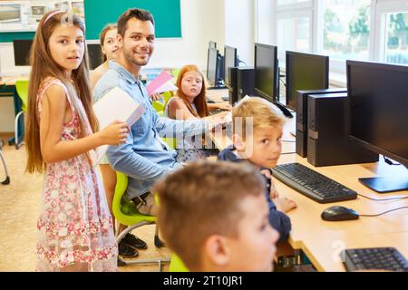 Portrait of smiling male and female students with teacher sitting in computer class Stock Photo